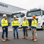 Quatre apprenants en tenue de sécurité se tiennent devant des poids lourds et un bâtiment de formation moderne à Arques, dans une ambiance pédagogique réaliste.