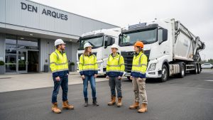Quatre apprenants en tenue de sécurité se tiennent devant des poids lourds et un bâtiment de formation moderne à Arques, dans une ambiance pédagogique réaliste.